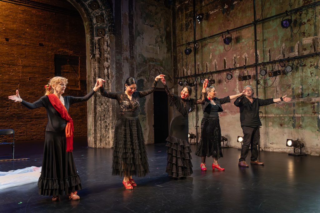 Five Flamenco X performers in black, sashed in red, hold hands and raise their arms on the Southern Theater stage